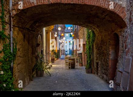 Italy, Province of Siena, Radicondoli, Lanterns illuminating old town alley with brick arch in foreground Stock Photo