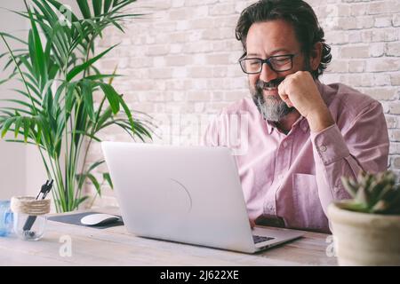 Smiling businessman wearing eyeglasses using laptop at home Stock Photo