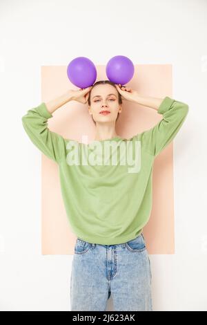 Beautiful woman holding purple balloons on head standing against white background Stock Photo