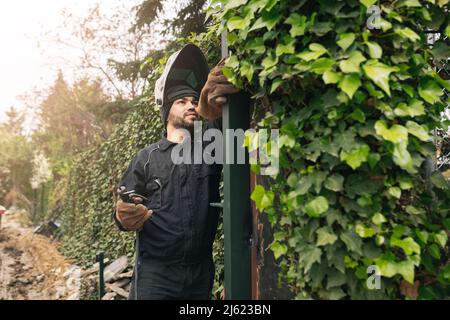 Welder with work tool working on metal gate at construction site Stock Photo