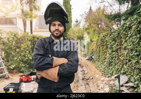 Welder wearing welding helmet standing with arms crossed at construction site Stock Photo