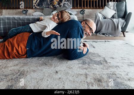 Smiling cute boy lying on grandfather's back at home Stock Photo