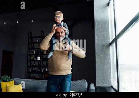 Senior man carrying cute grandson on shoulders at home