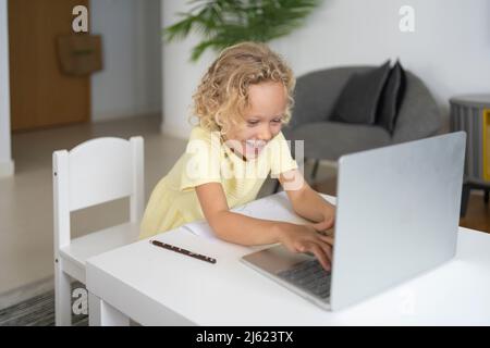 Happy blond girl using laptop sitting at table in living room Stock Photo