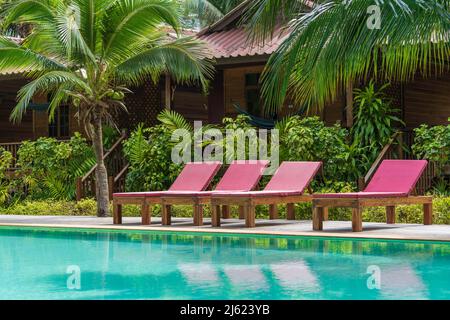 Swimming pool with relaxing beds and green palm trees in tropical garden on the island of Koh Phangan, Thailand