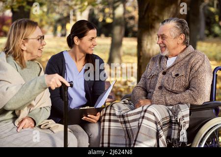 Smiling nurse discussing documents with senior couple at park Stock Photo