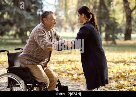 Nurse assisting senior disabled man standing up from wheelchair at park Stock Photo
