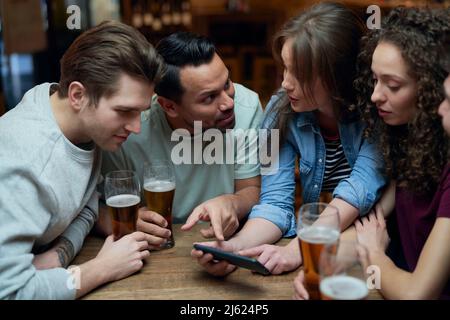 Group of friends having beer and sharing a smartphone in a pub Stock Photo