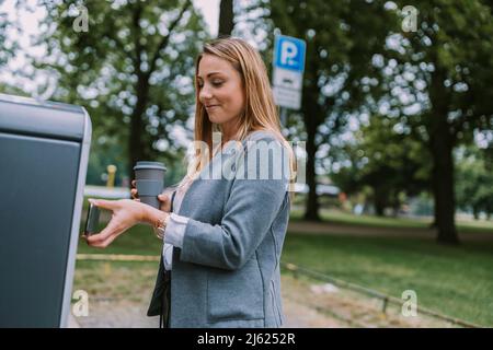 Woman paying bill through mobile phone at electric charging station Stock Photo