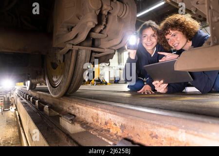 Engineer holding tablet PC analyzing monorail wheel with trainee in factory Stock Photo