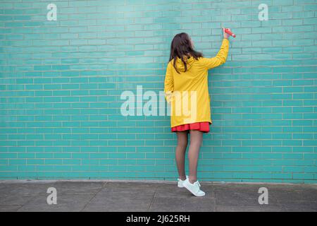 Young woman writing on brick wall standing on footpath Stock Photo