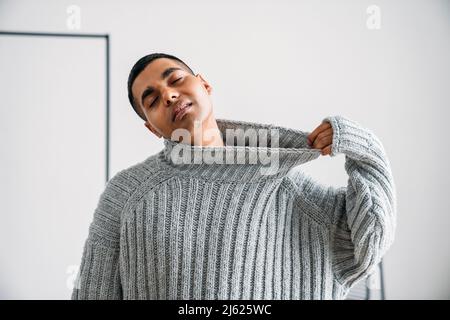 Young man with eyes closed pulling sweater in front of wall Stock Photo
