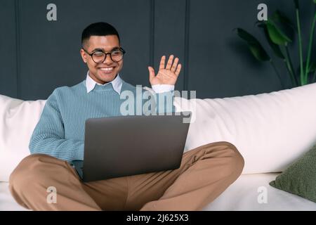 Happy freelancer waving hand on video call through laptop at home Stock Photo