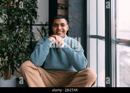 Smiling young man sitting by window at home Stock Photo