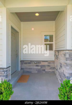 Vertical Entrance of a house with gray door on the side and two potted plants near the column posts Stock Photo