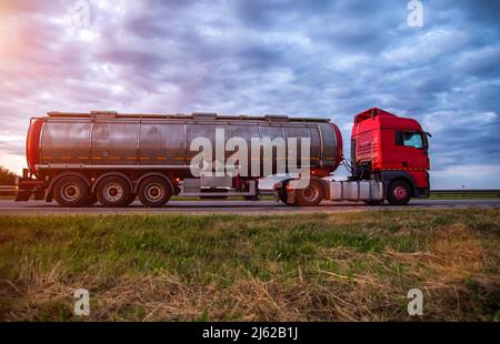 New red truck with a tanker truck transports gasoline against the background of the cloudy sky in the evening. Dangerous goods transport industry. Cop Stock Photo