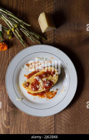 Corn polenta rolled with asparagus and topped with gravy and cheese flakes on white plate and dark wood background Stock Photo
