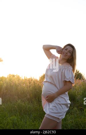 tender pregnancy portrait on sunset. expecting mother to be outside in pink dress. Beautiful tender mood photo of pregnancy Stock Photo