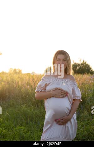 tender pregnancy portrait on sunset. expecting mother to be outside in pink dress. Beautiful tender mood photo of pregnancy Stock Photo