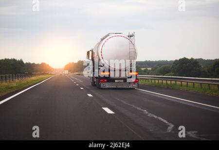 A truck with a semi-trailer transports a dangerous chemical cargo in a tank car on a highway against the background of a sunset. Sanctions in cargo tr Stock Photo