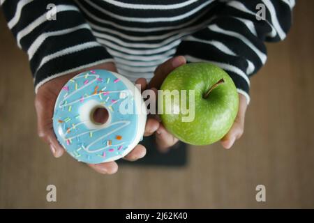 hand holding donuts and apple on hand on weight scale . Stock Photo