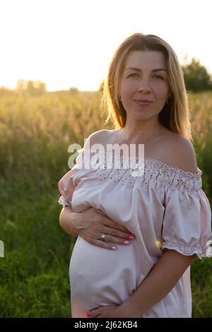 tender pregnancy portrait on sunset. expecting mother to be outside in pink dress. Beautiful tender mood photo of pregnancy Stock Photo