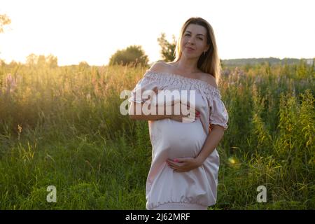 tender pregnancy portrait on sunset. expecting mother to be outside in pink dress. Beautiful tender mood photo of pregnancy Stock Photo