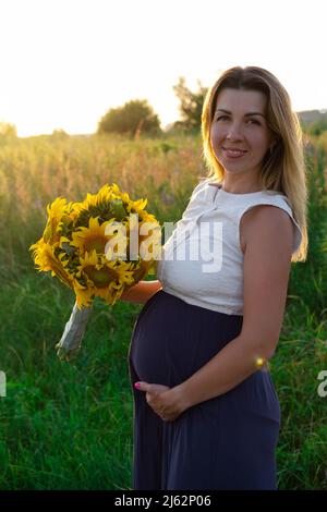 Happy healthy pregnancy and maternity. Portrait of pregnant young caucasian woman wearing long blue dress posing in park outside. Beautiful feminine e Stock Photo
