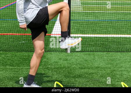 Side view of a high school boy standing in the A-position over small yellow hurdles on a green turf field while doing sports training drills and track Stock Photo