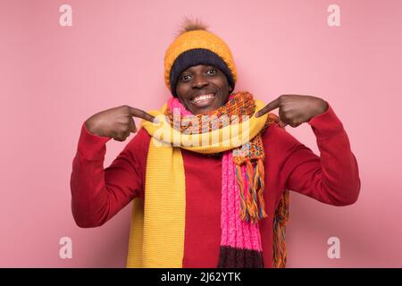 Cheerfull african man in warm clothes pointing on himself, smiling broadly. Studio shot Stock Photo