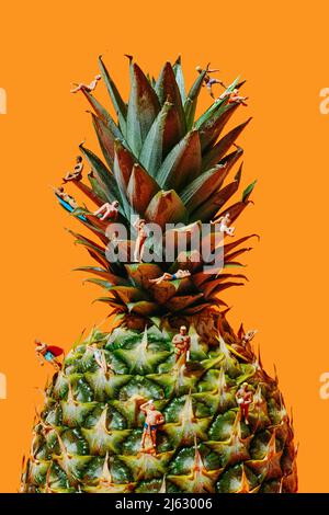 some miniature people, wearing swimsuit, in different actions, on a pineapple, against an orange background Stock Photo