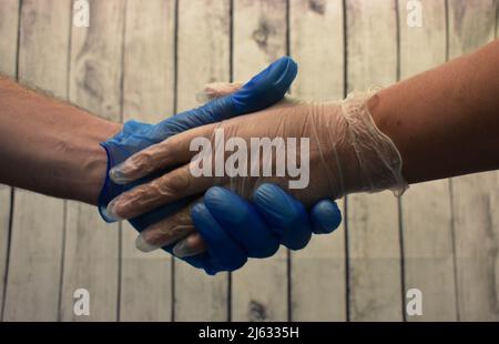 Two Adults/People Holding Hands But Wearing Latex Gloves Too Protect Themselves From Covid-19 Stock Photo