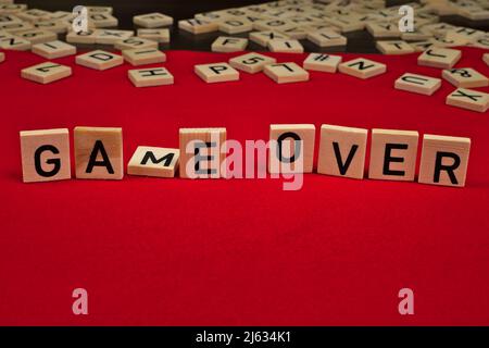 "Game over" phrase composed of wooden plates with letters on a red felt background Stock Photo