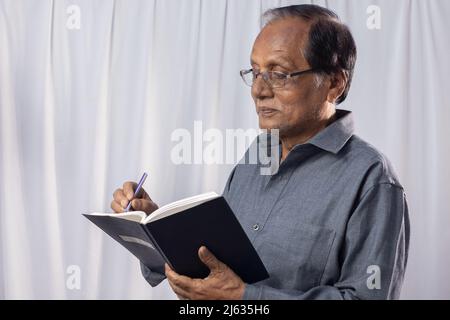 An old Indian man taking notes standing on white background Stock Photo