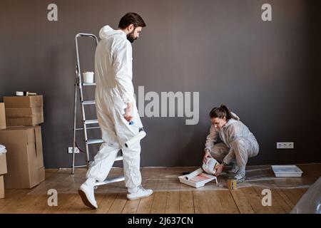 Modern young man and woman wearing protective clothes doing repair work in their apartment going to paint wall Stock Photo
