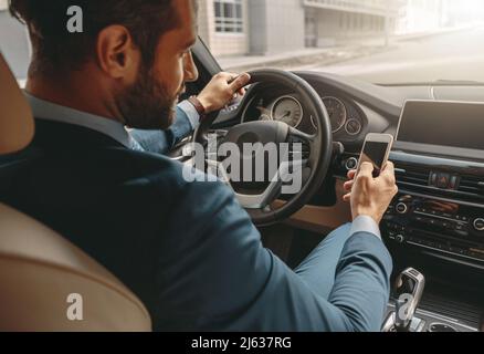Bearded seriously male holding cell phone during the driving a automobile Stock Photo