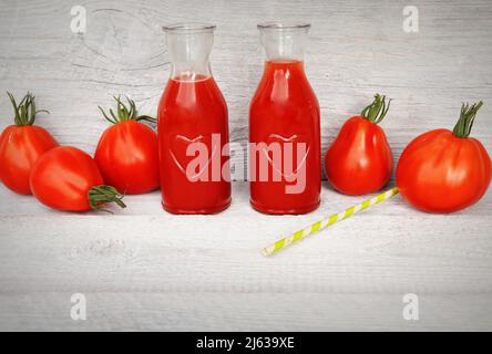 Two bottle of freshness juices on white wooden background with red tomatoes Stock Photo