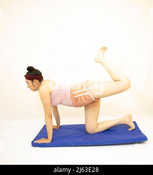 Beautiful young woman in yoga pose with one leg raised on blue mat Stock Photo