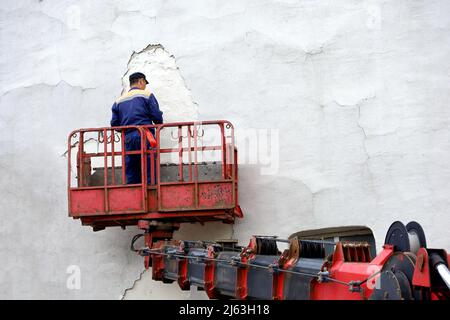 Worker in hydraulic lifting ramp repair the building wall. Builder on lifting platform plasters the facade, construction and repair works Stock Photo