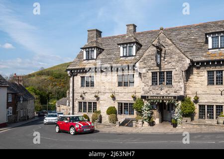 Red mini car driving through Corfe Castle village, Dorset, passing Bankes Arms Hotel in England, UK Stock Photo