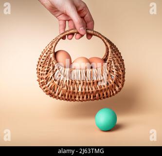 Hand with natural eggs in basket and outstanding Easter mint dyed one on beige background. Nutritious farm product and uniqueness, individuality concept. High quality photo Stock Photo