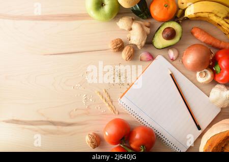 Vegetables on a wooden table and open notepad with empty leaf and pencil to score. Top view. Horizontal composition. Stock Photo