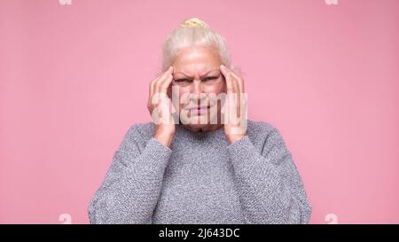 Senior woman suffering from headache desperate and stressed because of pain and migraine. She is holding hands on head. Stock Photo