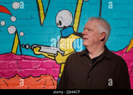A middle aged man standing in front of a wall that features colourful street art. Stock Photo