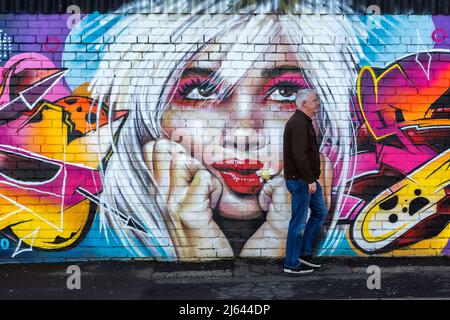 A middle aged man walking past a wall featuring colourful street art in an urban environment. Stock Photo