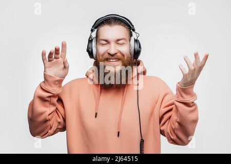 Scandinavian handsome surprised man laughs and listens to music in professional headphones isolated on gray background. Happy guy with ginger hairstyl