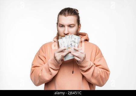 Handsome scandinavian man holding dollar currency money in his hands on gray background. Guy with ginger hairstyle and beard in a sweatshirt. The conc Stock Photo