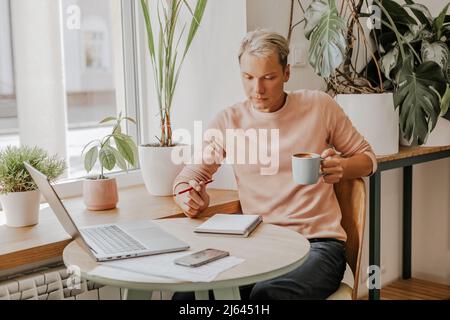 Man works in the workplace with documents and and drinks coffee in an eco cafe with plants Stock Photo