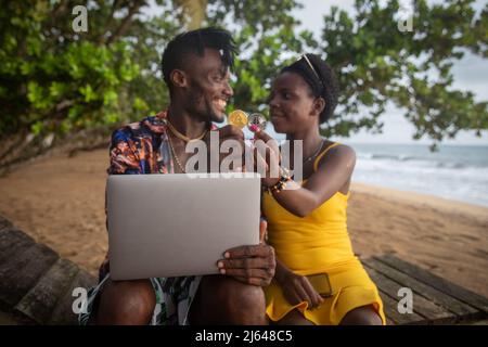 two african cryptocurrency investors on the beach hold a Bitcoin and Ethereum coin and use a laptop, concept of use of cryptocurrencies in africa Stock Photo