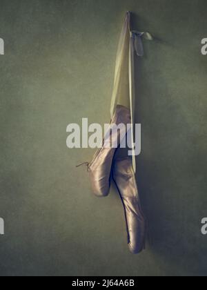 A pair of worn ballet pointe shoes hanging on a wall. Stock Photo